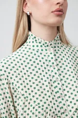 Camisa de viscosa blanca con estampa de lunares negros. Presenta cuello alto con volado y botonadura frontal, mangas largas con puños abullonados y frunces bajo el busto.