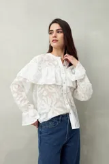 Camisa negra semitransparente de encaje bordado con diseño geométrico. Tiene silueta fluida, mangas largas y volados en el frente y los hombros.
