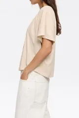 Remera negra de corte boxy con escote redondo, manga corta, logo estampado y pliegues en el hombro.