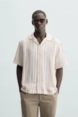 Camisa de hombre a rayas verticales color beige y blanco, de corte relaxed fit, manga corta y cuello bowling.