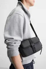 Bandolera negra de acabado engomado, con compartimento principal con cierre de cremallera y bolsillo interior con cremallera. Bolsillo frontal con cierre de hebilla de liberación rápida. Asa de hombro ajustable y extraíble.