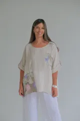 Blusa beige de lino con mangas 3/4 y apliques de tela estampada con motivos florales en bolsillo y parte inferior.