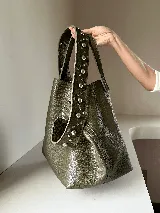 Cartera tipo tote bag color bordó, confeccionada en cuero con textura granulada. Tiene doble asa corta de mano y asa larga extraíble con diseño de tachas para usar como bandolera.