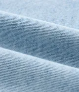 Camisa de jean de algodón, color celeste claro lavado, con cuello tradicional, manga larga y bolsillo de parche en el pecho. Presenta un cierre frontal con botones metálicos.