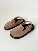 Zuecos color beige de cuero gamuzado, con punta cerrada, suela de goma negra y tira trasera con hebilla metálica.