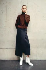 Falda midi de punto color gris oscuro, de tiro alto con cintura elástica, corte pareo cruzado con botón dorado y bajo asimétrico.