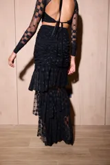 Falda larga de color negro confeccionada en microtul y encaje. Presenta un diseño con frunces en la zona de la cadera, volados escalonados que aportan movimiento y una abertura lateral pronunciada. Cuenta con forrería interna en la parte superior.