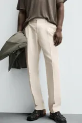 Pantalón de vestir color beige claro, corte regular fit, con pliegues frontales, bolsillos laterales y bolsillos traseros de vivo.