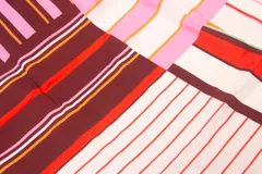 Pareo rectangular de viscosa con estampado de flores rojas sobre fondo borgoña y borde inferior con rayas verticales rojas, amarillas y blancas.