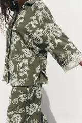 Camisa verde militar con bordado floral blanco, cuello solapa, escote en pico, manga tres cuartos con detalle de guipur y cierre frontal con botones.
