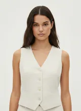 Chaleco sastrero color crema confeccionado en tejido liviano de viscosa y lino, con cierre de botones y bolsillos frontales.