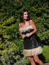 Vestido corto de fiesta con lentejuelas negras y flecos dorados en el escote y el ruedo.
