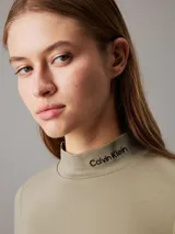 Remera color verde oliva de punto milano con cuello perkins y mangas largas. Tiene el logo de Calvin Klein bordado en el cuello.