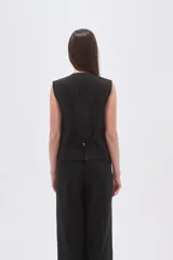 Chaleco negro con finas rayas verticales blancas (pinstripe), escote en V y cierre frontal de botones. Presenta bolsillos ribeteados en la parte inferior delantera.