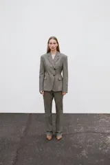 Blazer gris jaspeado de cuello solapa y manga larga con hombreras. Tiene bolsillos delanteros con solapa y cierre frontal cruzado con botones.