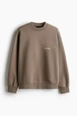 Buzo de algodón pesado color marrón con efecto lavado e interior cepillado suave. Modelo con diseño estampado, cuello redondo y hombros caídos. Remate acanalado en cuello, puños y bajo. Corte holgado.