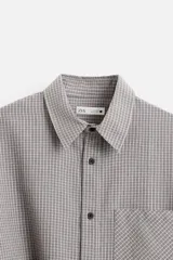 Camisa de hombre relaxed fit con cuello solapa, manga larga con puño abotonado, bolsillo de parche en el pecho y cierre frontal con botones. Diseño a cuadros en tonos gris y blanco.