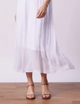 Vestido largo blanco de crepe, con escote redondo y sobrecapa con ruedo de broderie. Corte en la cintura con punto smock.