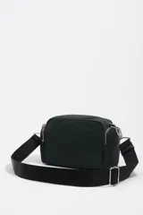 Bolso bandolera de nylon color verde oscuro, con estructura blanda y múltiples compartimentos con cierre de cremallera. Presenta correa ajustable de tejido negro y logo metálico con el texto "BIMBA Y LOLA" en blanco en el frente.