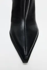Botín negro de cuero con tacón fino, punta fina y cierre lateral con cremallera.