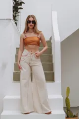 Pantalón jean wide leg color crudo con costuras rojas y ruedo desflecado.