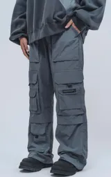 Pantalón gris de corte oversize, estilo cargo, con cintura elástica, múltiples bolsillos y detalles reflectivos.