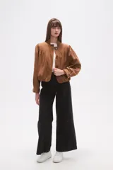 Campera marrón de manga larga con cuello mao y cierre frontal de un solo botón. Presenta pinzas y frunces en el canesú delantero y en los hombros, creando un efecto abullonado en las mangas. El bajo es ajustado con elástico.