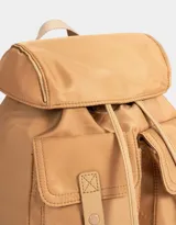 Mochila de tela color lila, con solapa con broche y tira de ajuste, doble bolsillo frontal con broche y pouch con charm lateral en forma de cartera.