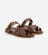 Sandalia plana marrón de cuero sintético, con punta redonda, tiras cruzadas y hebilla dorada lateral.