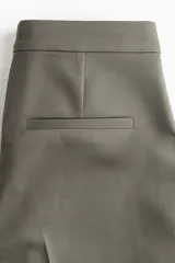Pantalón cigarette tobillero color verde oliva, con cintura estándar, cierre y pretina prolongada con corchete oculto. Piernas ajustadas con abertura corta en los bajos, bolsillos al bies y bolsillo de atrás decorativo. Pliegues adelante y atrás.