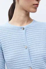 Chaqueta de punto color celeste claro, de manga larga y corte ajustado, con cuello redondo y cierre frontal de botones metálicos plateados. El tejido presenta un patrón texturizado horizontal.