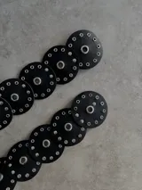 Cinturón negro de eco cuero con apliques circulares y ojalillos metálicos.