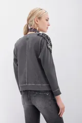 Buzo gris de algodón rústico con mangas dolman y cuello redondo. Apliques bordados con mostacillas y lentejuelas en los hombros.