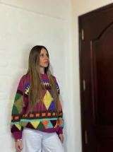 Sweater de lana merino color crema con cuello alto y diseño con motivos geométricos en amarillo, naranja, violeta y negro.