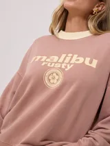 Sweater color ladrillo con cuello redondo en color crema. Estampado frontal con el texto 'Malibu Rusty' y un logo con forma de flor. Corte holgado.