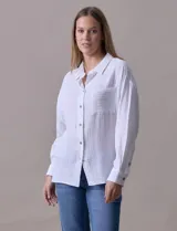 Camisa blanca de algodón con textura arrugada, cuello con solapa, abertura central con botones y bolsillo aplicado en el pecho. Mangas largas con largo regulable mediante presilla y botón.