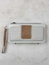 Billetera mediana de cuero color blanco y marrón con cierre de cremallera, compartimentos internos y correa de muñeca.