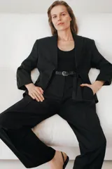 Pantalón negro de tiro medio con cintura con trabillas, bolsillos laterales y con solapa en espalda. Detalle de pinzas y raya planchada en delantero. Cierre frontal con cremallera, botón y ganchos metálicos.