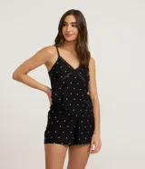 Pijama short doll femenino compuesto por una musculosa y un short. La musculosa es de breteles finos ajustables, escote en V con detalle de encaje cruzado en el busto. El short es corto con cintura elástica. Estampado de lunares blancos sobre fondo negro.