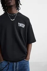 Sudadera negra de corte holgado con cuello redondo y mangas cortas. Estampa frontal y trasera con gráficos y textos en color blanco.
