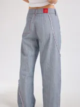 Pantalón largo de tiro medio alto a rayas verticales azules y blancas con costuras rojas a contratono. Presenta bolsillos delanteros y traseros, y cortes con desflecado.