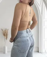 Top tipo pañuelo de crochet tejido a mano, color beige, con escote halter anudado al cuello y diseño triangular que deja el abdomen al descubierto.