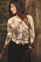 Chaqueta color crema de tejido de punto calado, con cuello redondo, manga larga y cierre frontal con botones.
