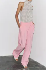 Pantalón rosa de tiro medio con trabillas en la cintura, bolsillos laterales, pinzas delanteras y pierna ancha. Cierre frontal con cremallera, botón y ganchos metálicos.