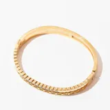 Pulsera rígida dorada con doble banda, una con diseño calado y otra con incrustaciones de strass.