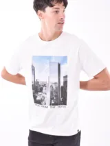 Remera blanca de corte recto con estampa fotográfica de edificios en la parte frontal.