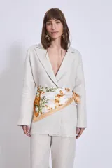 Blazer color crema de lino con corte clásico, solapas de muesca y cierre cruzado con un botón. Incluye un pañuelo de seda estampado atado a la cintura.