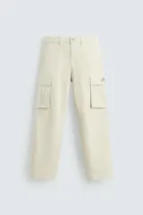 Pantalón cargo color beige de corte relaxed fit, confeccionado en tejido de algodón con elasticidad. Cuenta con bolsillos frontales, traseros y bolsillos tipo parche con solapa en los laterales.