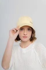 Gorra de béisbol color amarillo pastel, con visera curva y logo de Peach bordado en el frente. Ajustable en la parte trasera.