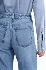 Pantalón de jean celeste de tiro alto, corte ancho y recto, con cinco bolsillos y cierre con botón.